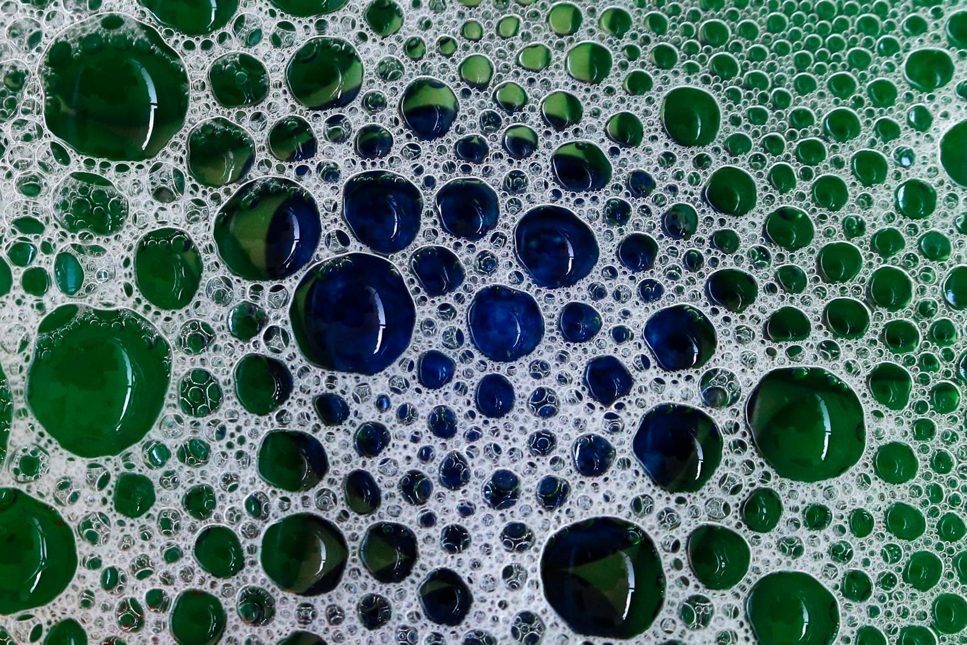 Close-up of vibrant soap bubbles creating a green and blue abstract pattern.