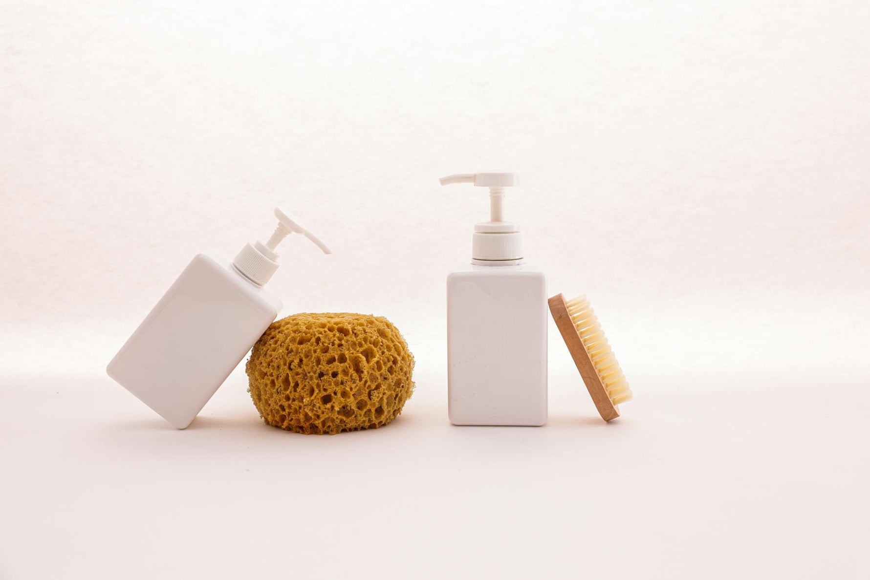 Clean white pump bottles paired with a sponge and brush for a simple bathroom elegance.