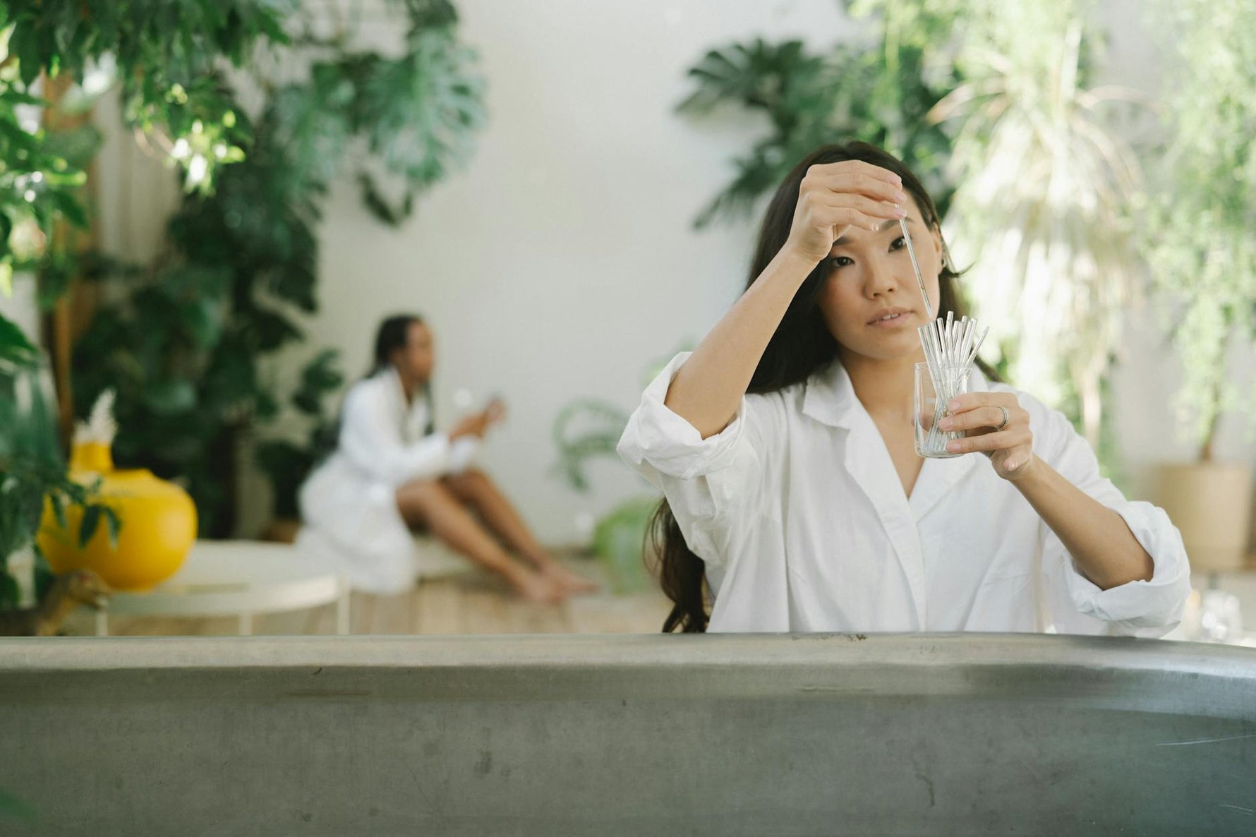 A woman works with glassware in a serene, plant-filled setting, creating a balanced, natural ambiance.