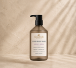 A bottle of Good Life Rituals Good Body Wash in Jasmine + Neroli, featuring a frosted amber-brown bottle and a black pump dispenser, set against a textured beige background with soft diagonal shadows.