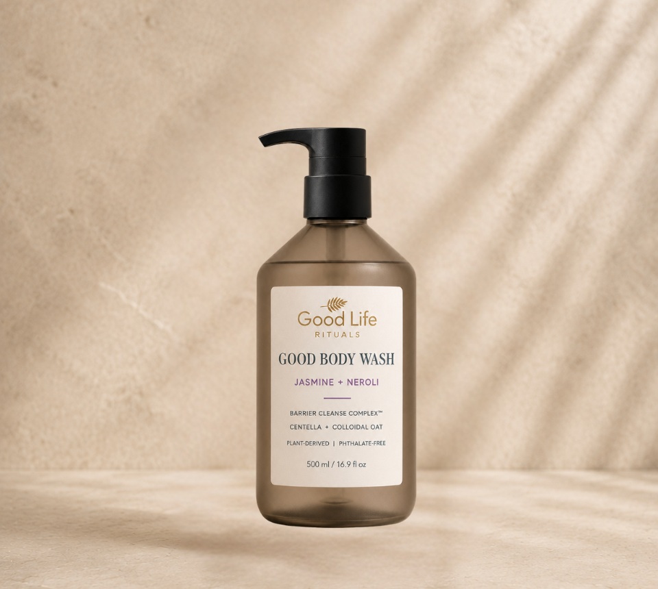 A bottle of Good Life Rituals Good Body Wash in Jasmine + Neroli, featuring a frosted amber-brown bottle and a black pump dispenser, set against a textured beige background with soft diagonal shadows.